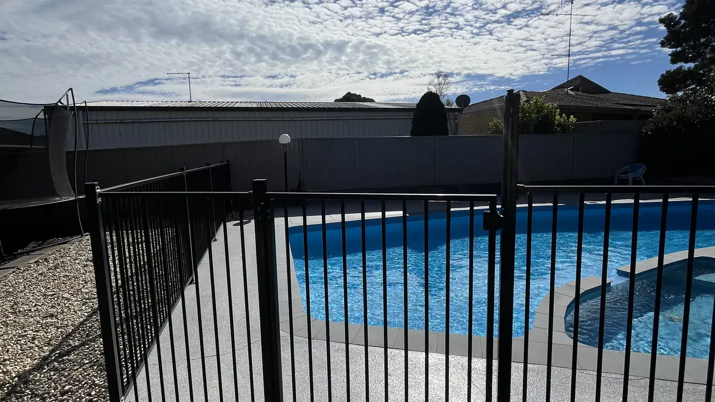 A pool enclosed by a black aluminium pool safety fence on a paved deck in bright sun