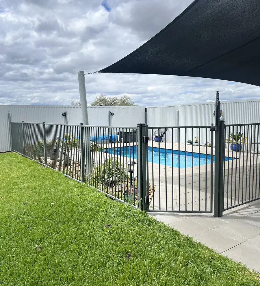 A black aluminium pool safety fence and gate, with a shade sail over the pool