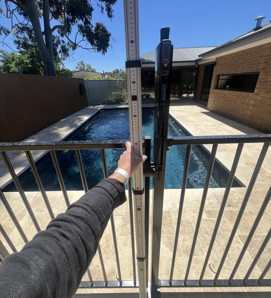 Leanne measuring a pool safety gate with a gauge during an inspection, the pool behind