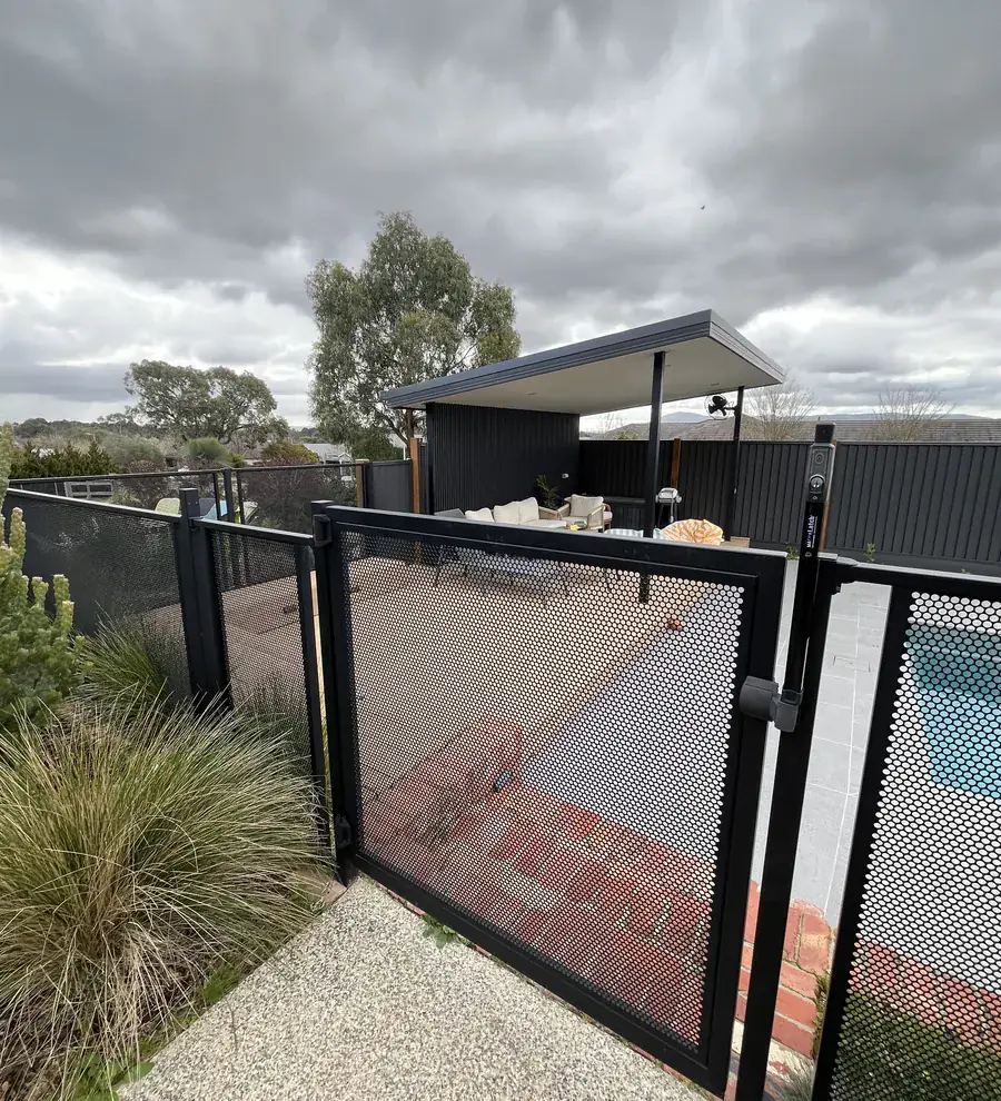 A black steel mesh pool safety gate, with the pool behind