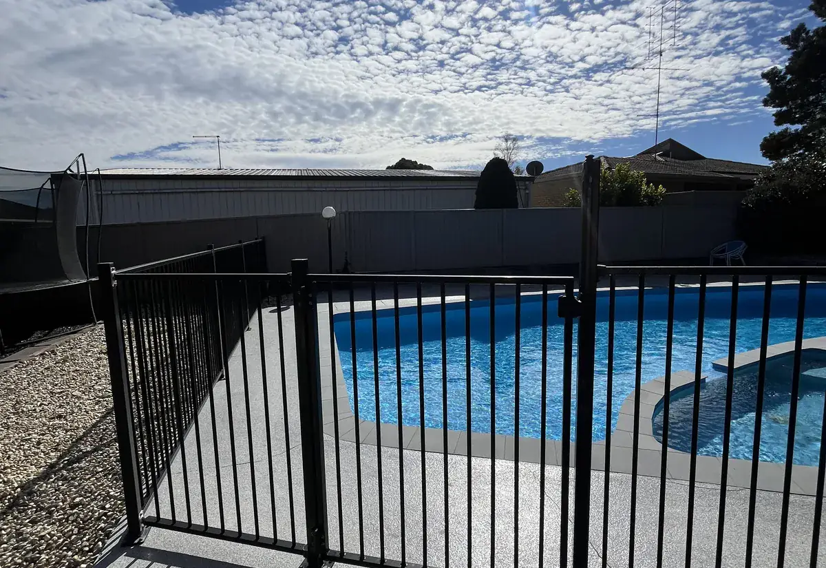 A black aluminium pool safety fence on a paved deck beside a pool