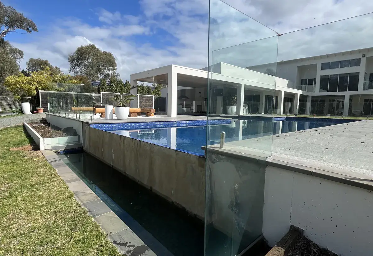 A frameless glass pool safety fence beside a modern home, with an infinity-edge pool