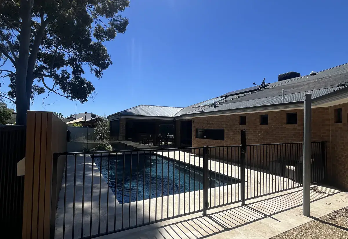 A black aluminium pool safety fence around a pool, with a gum tree and home behind